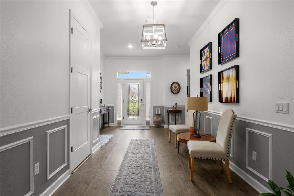 A bright entryway features wood-look flooring, wainscoting, two chairs, and a glass-paneled front door — 1720 VERDE DRIVE, CLEARWATER, FL