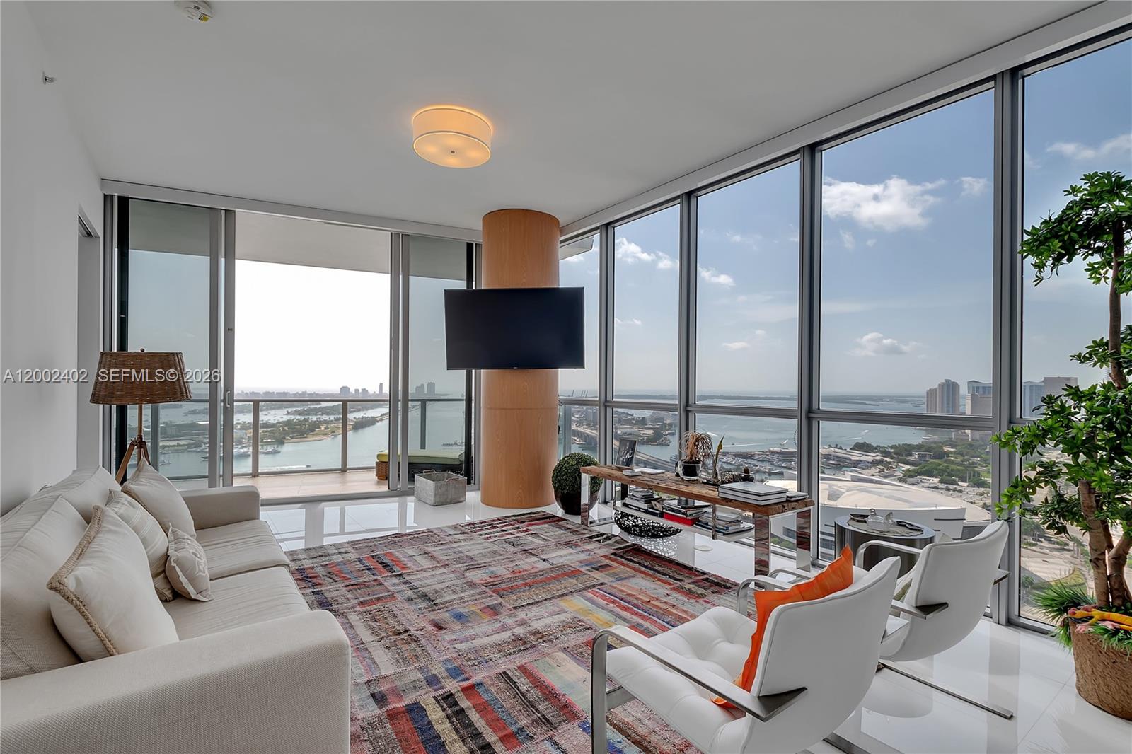 A living room with floor-to-ceiling windows, a central column with a television, and water views — 1100 Biscayne Blvd # 3901, Miami FL 33132, MIAMI, FL