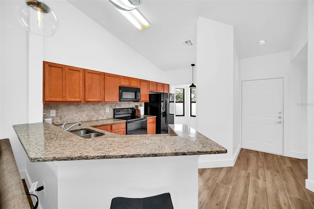 A kitchen features wood cabinets, granite countertops, a breakfast bar, and stainless steel appliances — 7823 SUGAR BEND DRIVE UNIT 7823, ORLANDO, FL