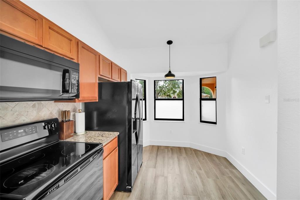 A kitchen with wood cabinets, stainless steel appliances, and a dining nook with large windows — 7823 SUGAR BEND DRIVE UNIT 7823, ORLANDO, FL