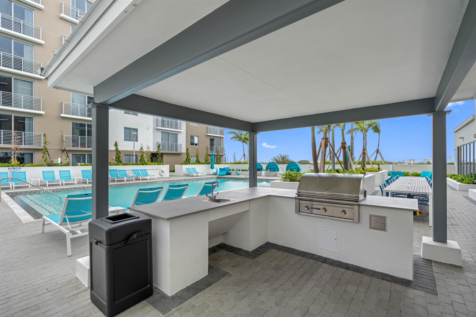 An outdoor kitchen with a grill and sink overlooks a swimming pool and apartment building — 200 NE 1st Avenue # 633, Pompano Beach FL 33060, POMPANO BEACH, FL