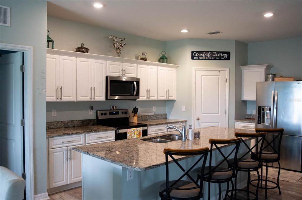 A kitchen features white cabinets, granite countertops, a center island with seating, and stainless appliances — 3021 BLUE SHORES WAY, NEW SMYRNA BEACH, FL