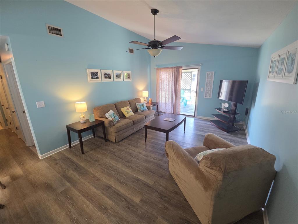 A living room with light blue walls, wood-look flooring, a sofa, armchair, and sliding doors — 644 16TH STREET, PANAMA CITY BEACH, FL