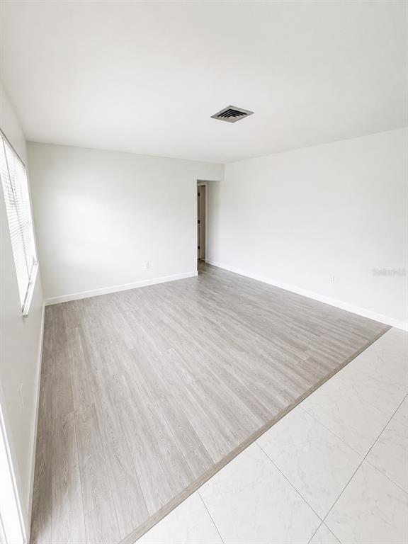 An empty room features light wood-look flooring, white walls, and a white tiled entryway — 2428 LINWOOD DRIVE, SARASOTA, FL
