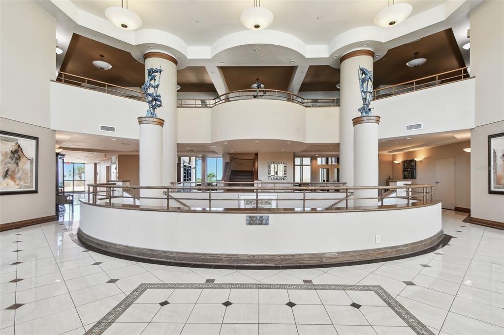 A spacious lobby features a curved balcony, tall columns with dolphin sculptures, and tiled floors — 1560 GULF BOULEVARD UNIT 306, CLEARWATER BEACH, FL