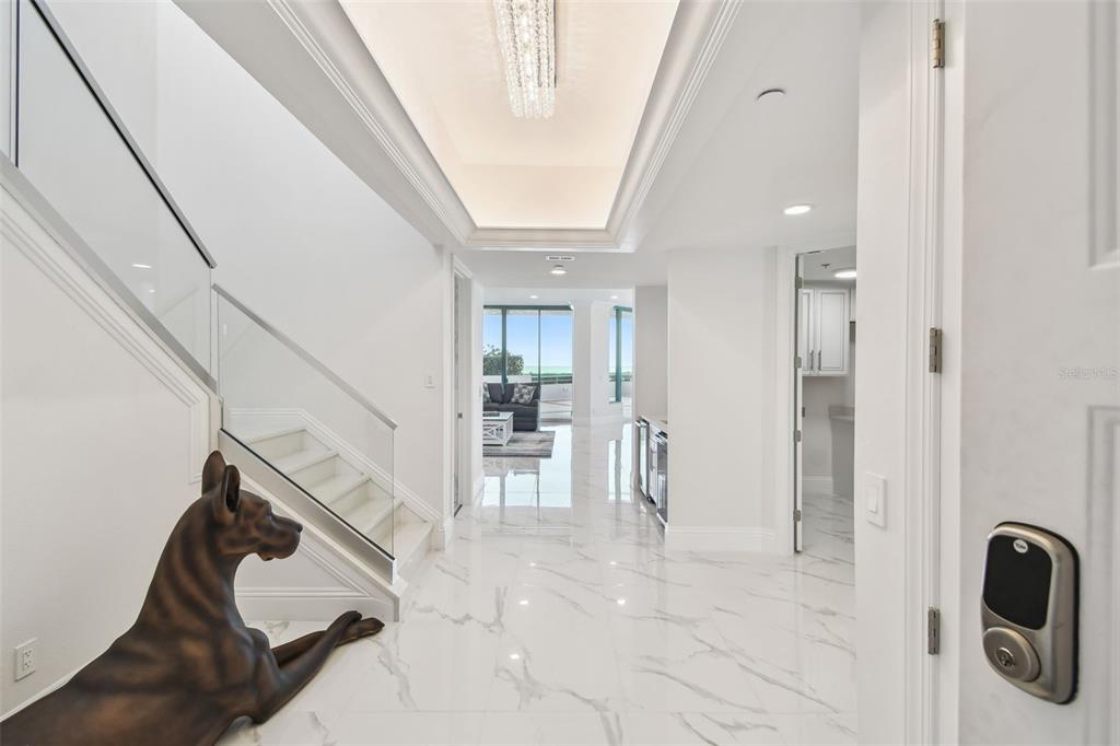 A bright entryway features white marble floors, a glass-railed staircase, and a large dog statue — 1560 GULF BOULEVARD UNIT 306, CLEARWATER BEACH, FL