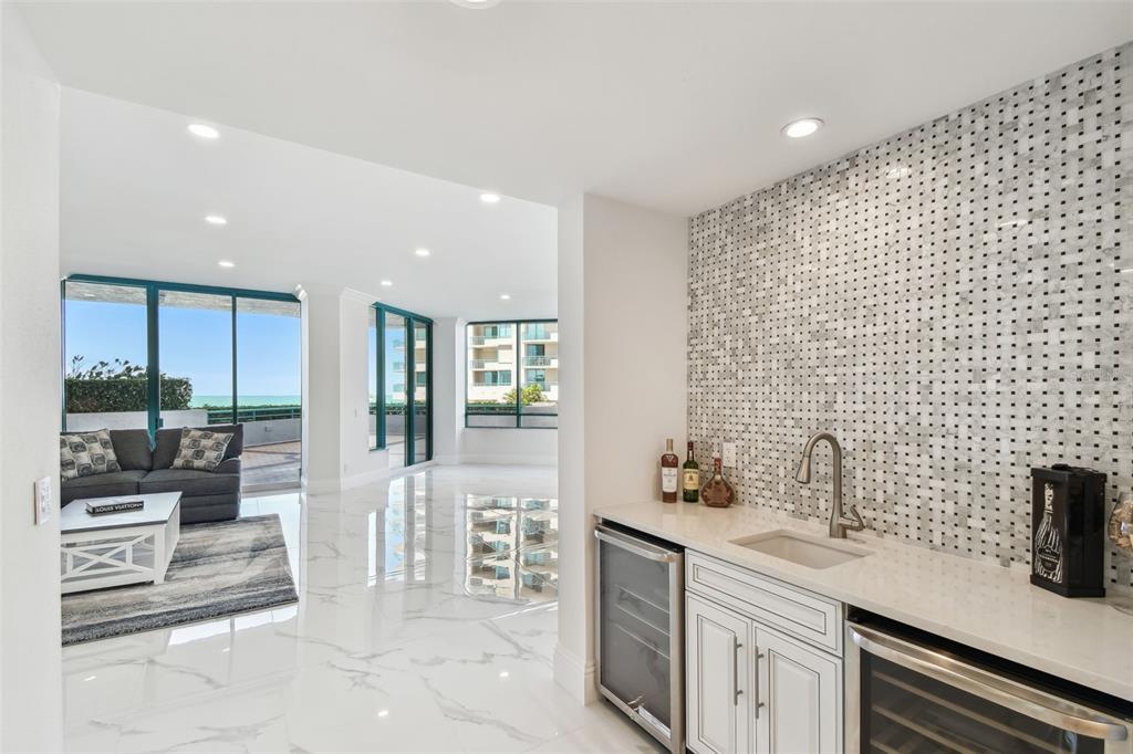 A wet bar with white cabinetry and a mosaic backsplash overlooks a bright living area — 1560 GULF BOULEVARD UNIT 306, CLEARWATER BEACH, FL