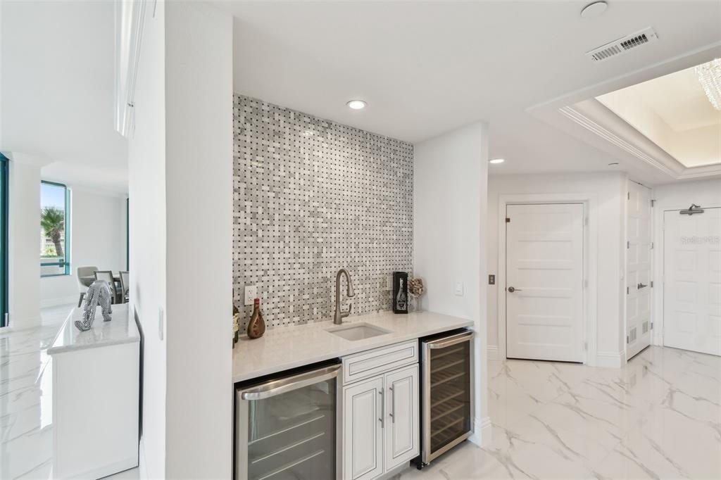 A wet bar features a mosaic tile backsplash, white cabinetry, and two under-counter wine refrigerators — 1560 GULF BOULEVARD UNIT 306, CLEARWATER BEACH, FL
