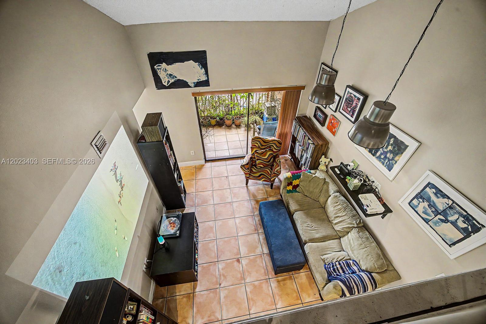 A high-angle view of a living room with tiled floors, a projector screen, and balcony access — 10233 NW 9th St Cir # 1, Miami FL 33172, MIAMI, FL