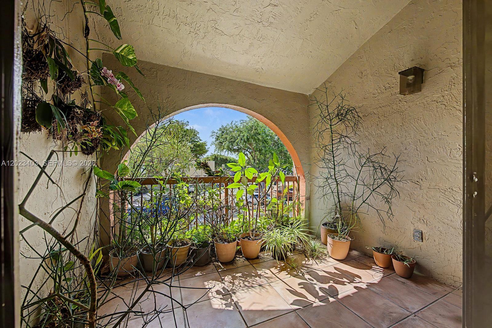 A covered balcony features a large arched opening, tiled flooring, and numerous potted plants — 10233 NW 9th St Cir # 1, Miami FL 33172, MIAMI, FL