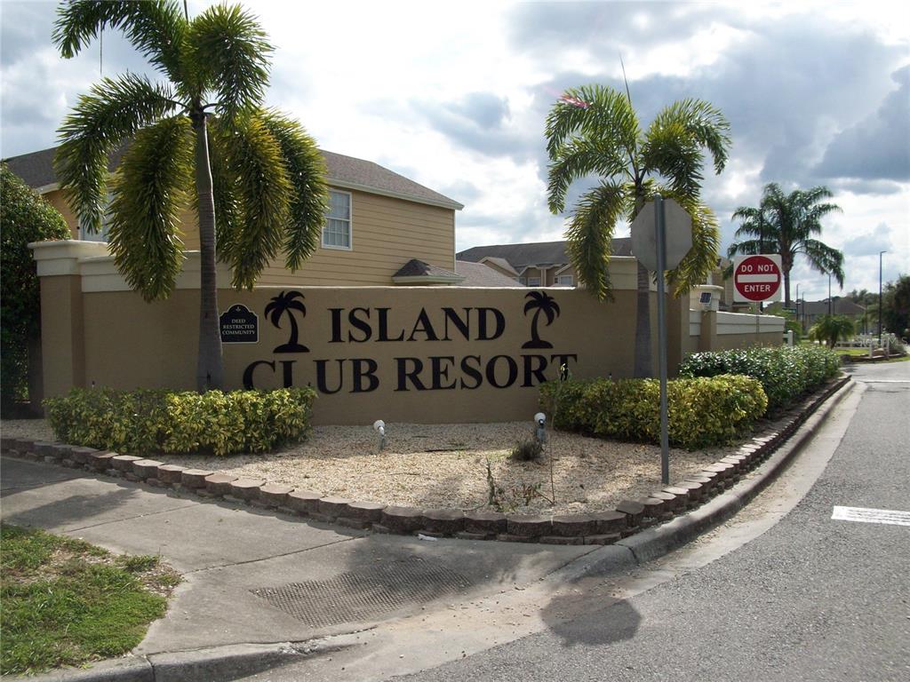 A tan stucco sign for Island Club Resort stands near a road with palm trees — 511 COCONUT PALM WAY, DAVENPORT, FL
