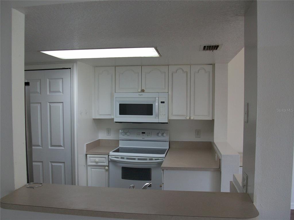 A kitchen features white cabinets, a white stove, a microwave, and tan countertops — 511 COCONUT PALM WAY, DAVENPORT, FL