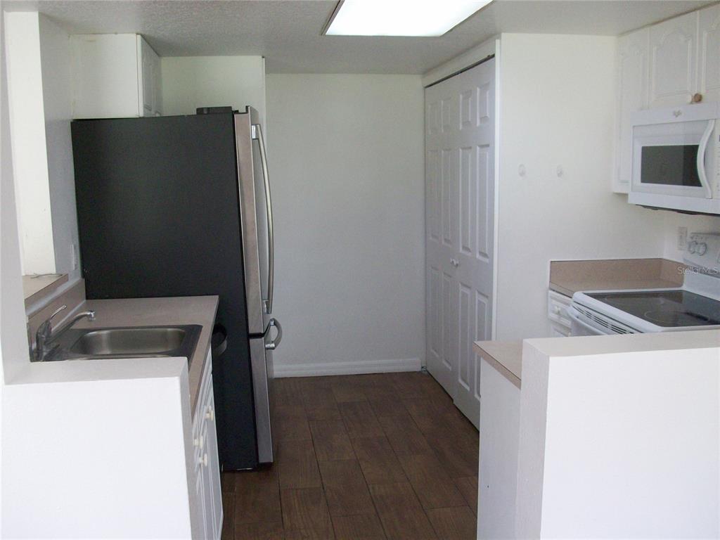 A kitchen features white cabinets, a black refrigerator, a stainless steel sink, and wood-look flooring — 511 COCONUT PALM WAY, DAVENPORT, FL