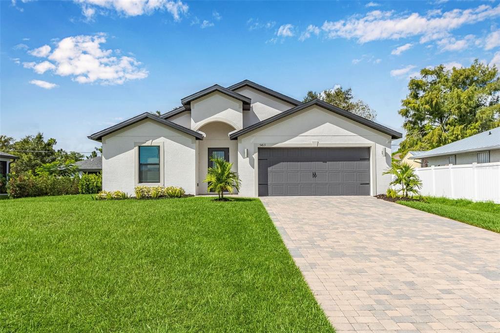 A single-story house with a white stucco exterior, gray garage door, and a paver driveway — 5413 DAYTON LANE, PORT CHARLOTTE, FL