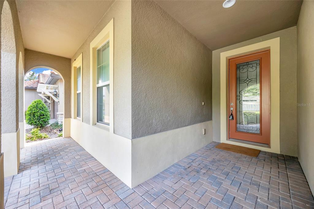 A covered entryway features a brick paver floor, a tan stucco wall, and a glass-paneled door — 10713 BERRY CREEK ROAD, ORLANDO, FL