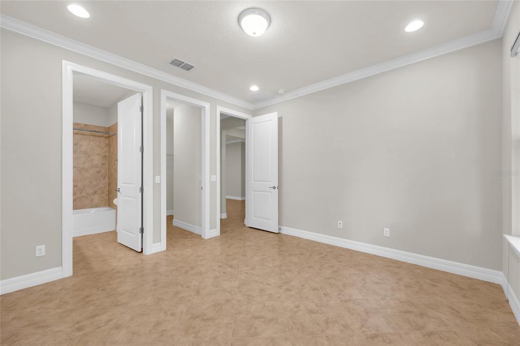 An empty room with beige tile flooring, white walls, crown molding, and three interior doors — 10713 BERRY CREEK ROAD, ORLANDO, FL
