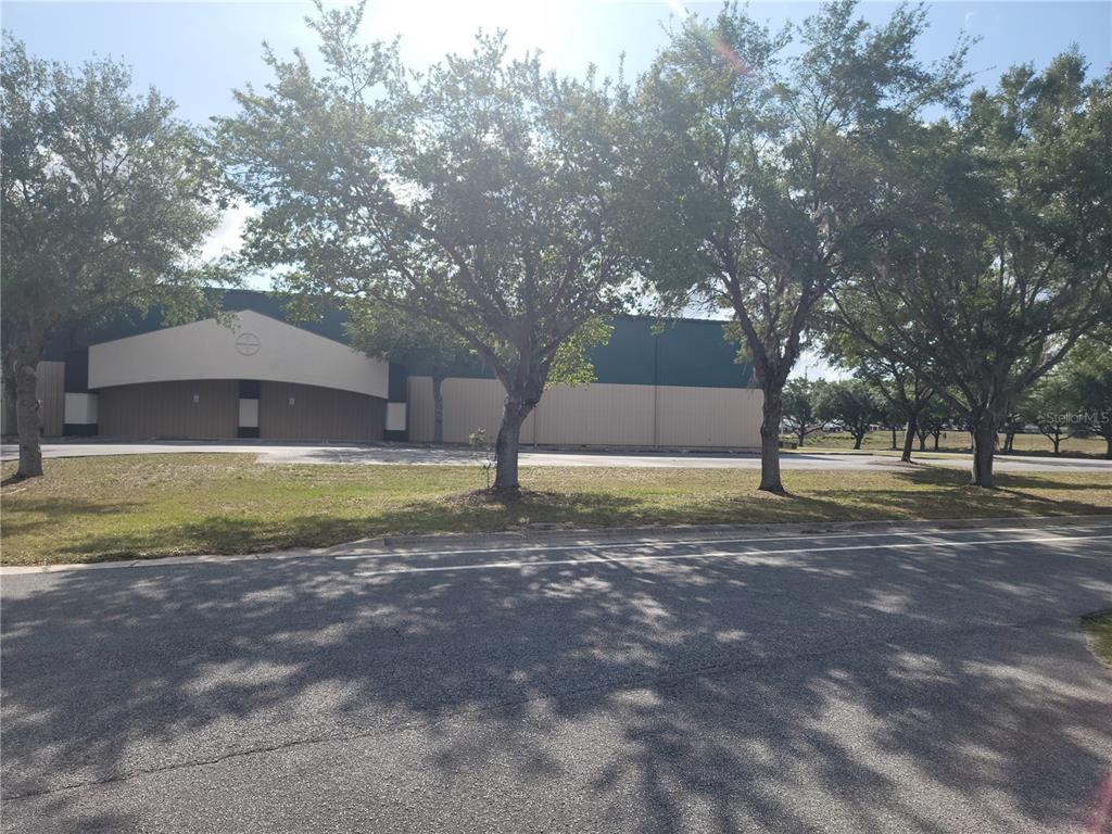 A large commercial building with a tan and green exterior stands behind several mature trees — 1501 SW 44TH AVENUE, OCALA, FL
