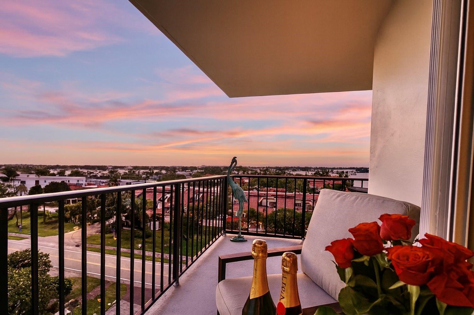 A balcony with a metal railing overlooks a sunset view with roses and champagne bottles — 3460 S Ocean Boulevard # 608, Palm Beach FL 33480, PALM BEACH, FL