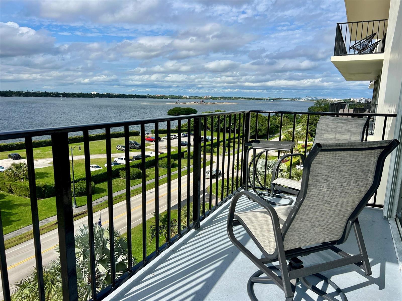 A balcony with two chairs overlooks a road, green space, and a large body of water — 3460 S Ocean Boulevard # 608, Palm Beach FL 33480, PALM BEACH, FL