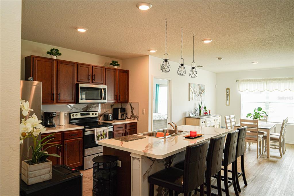 A kitchen features dark wood cabinets, a marble-topped island with seating, and stainless steel appliances — 3184 ROYAL TERN DRIVE, WINTER HAVEN, FL