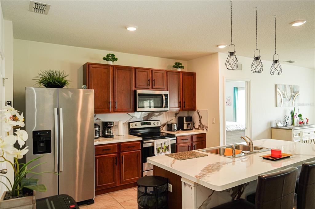 A kitchen with wood cabinets, stainless steel appliances, and a large white marble-topped island — 3184 ROYAL TERN DRIVE, WINTER HAVEN, FL