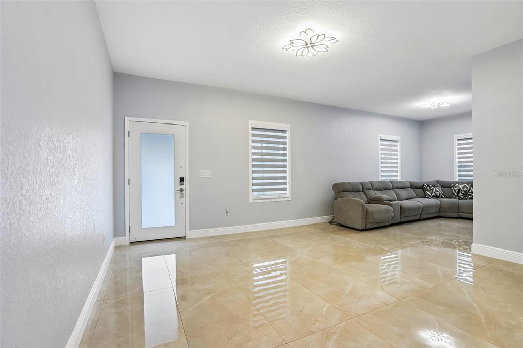 A living room with light gray walls, large beige floor tiles, and a gray sectional sofa — 2703 AUBURN AVENUE W, TAMPA, FL