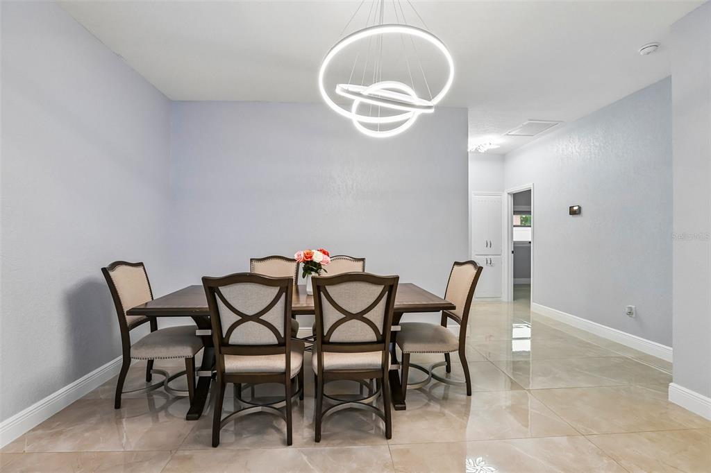 A dining room features a modern circular chandelier, a wooden table, and six upholstered chairs — 2703 AUBURN AVENUE W, TAMPA, FL
