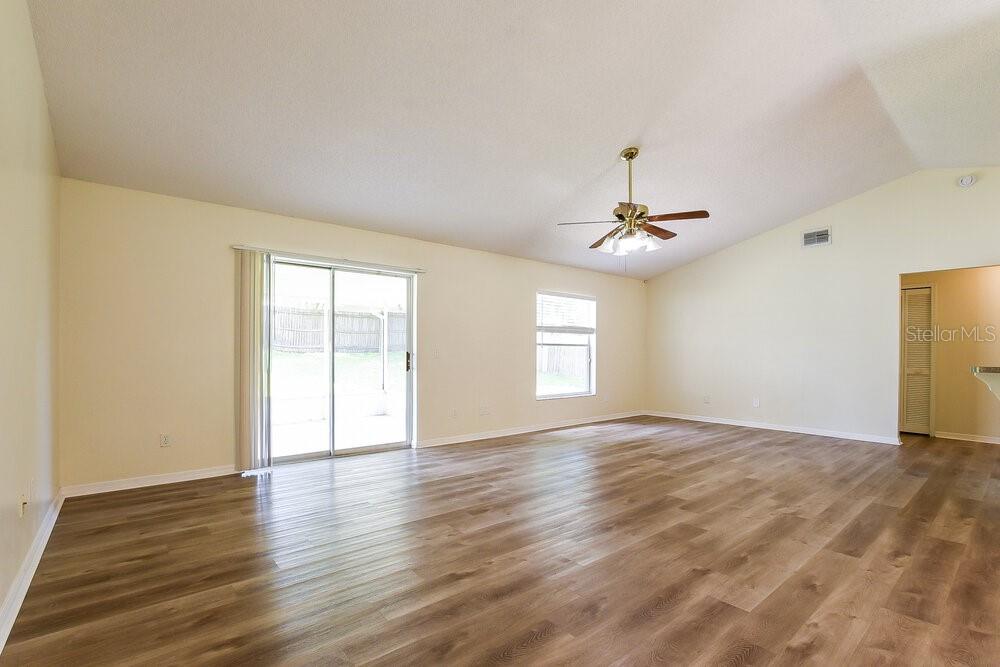 An empty living room features light-colored walls, wood-look flooring, a ceiling fan, and sliding doors — 2556 COACHBRIDGE COURT, OVIEDO, FL