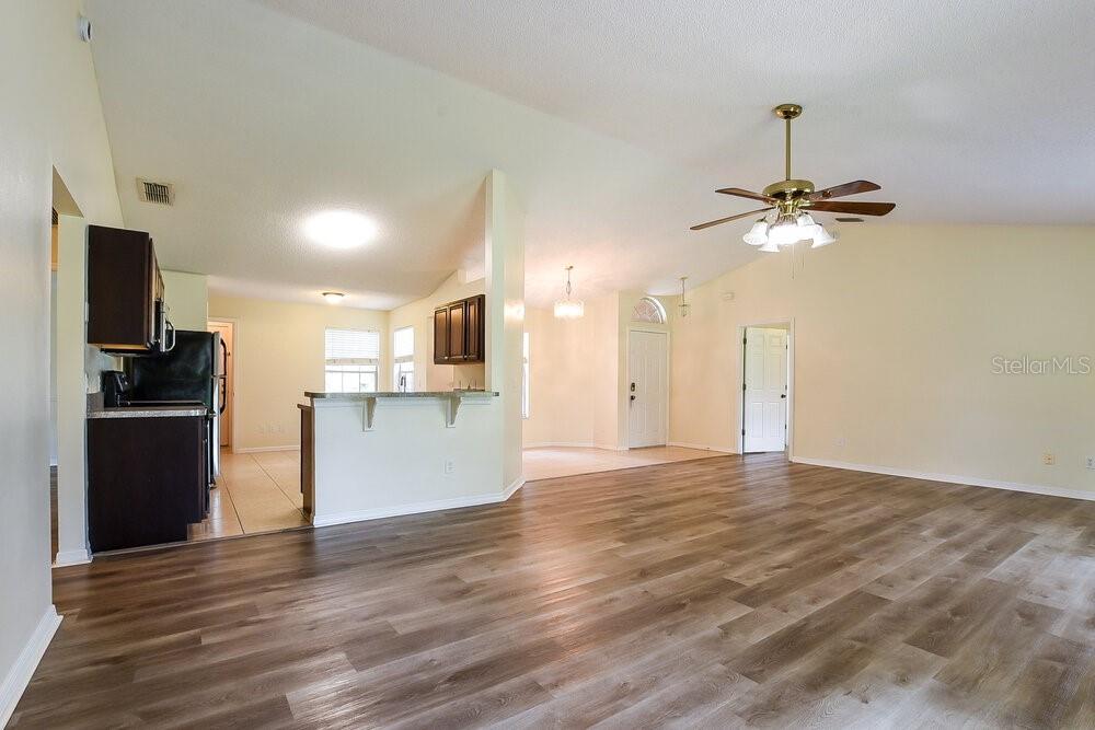 An open-concept living area features wood-look flooring, a kitchen with dark cabinets, and vaulted ceilings — 2556 COACHBRIDGE COURT, OVIEDO, FL