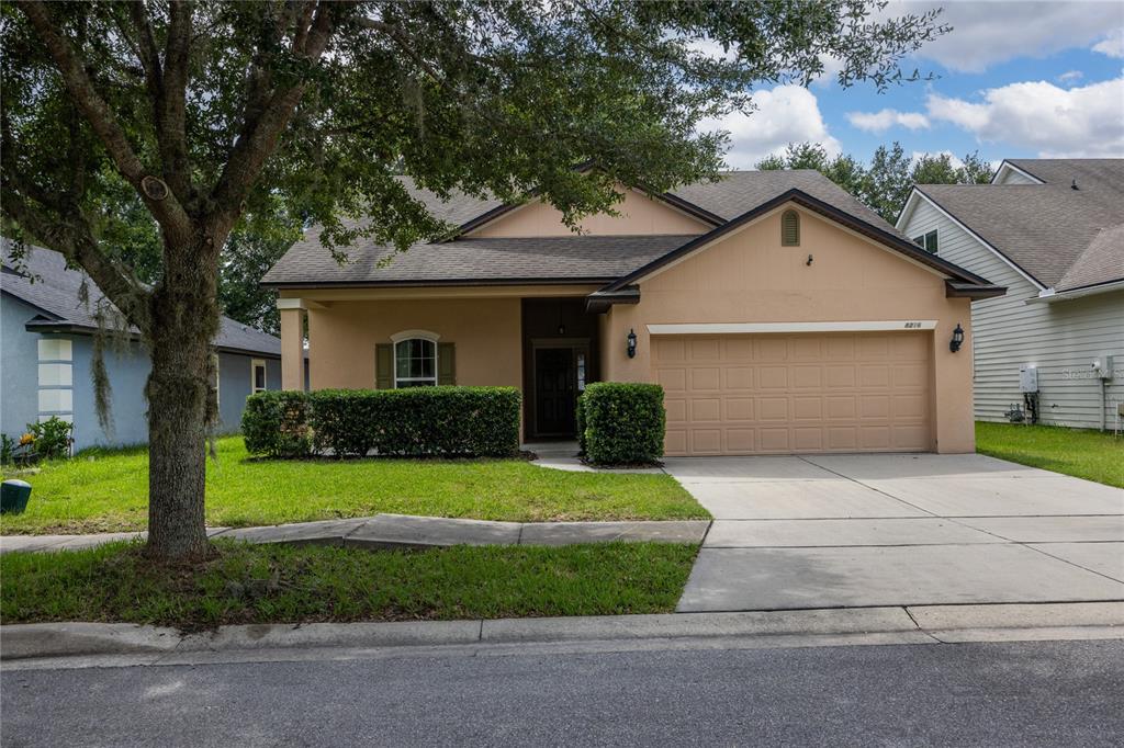 A single-story tan house with a two-car garage and a front lawn with trees — 8216 NW 54TH STREET, GAINESVILLE, FL