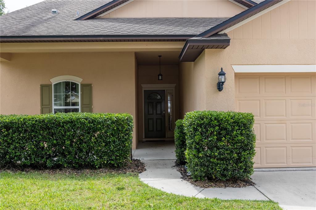 The exterior of a tan house features a front door, a garage, and manicured hedges — 8216 NW 54TH STREET, GAINESVILLE, FL