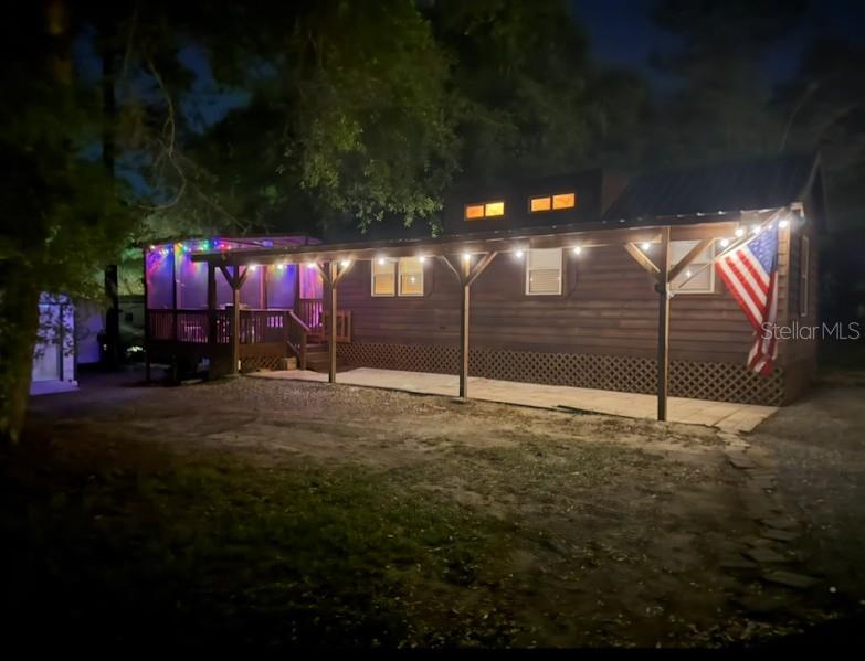 A wooden cabin at night features a covered porch with string lights and an American flag — 25235 142ND LANE NE UNIT 185, FORT MC COY, FL