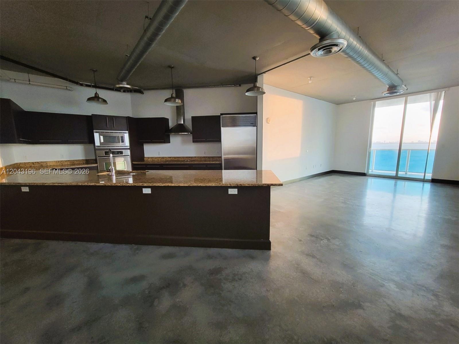 A modern kitchen with dark cabinets and granite countertops opens to a spacious living area — 700 NE 25th St # 1004, Miami FL 33137, MIAMI, FL