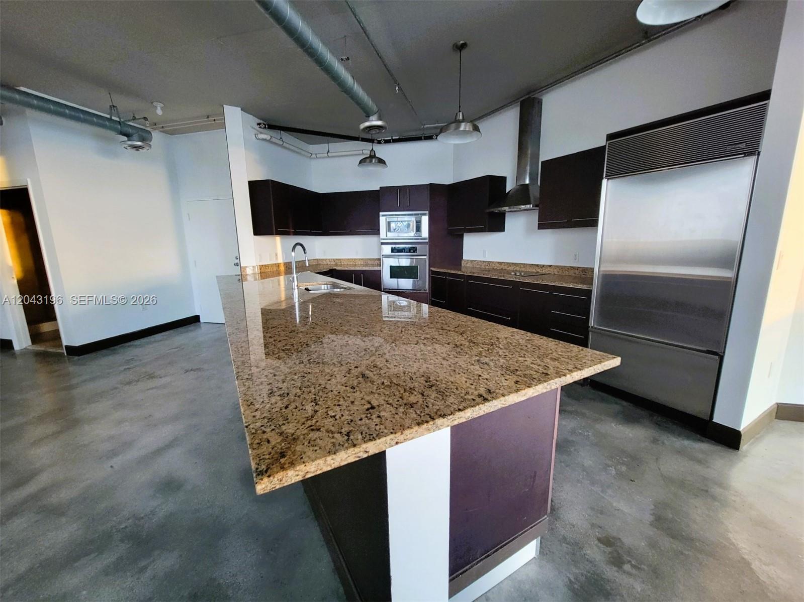 A modern kitchen features dark cabinets, granite countertops, a large island, and exposed industrial ductwork — 700 NE 25th St # 1004, Miami FL 33137, MIAMI, FL