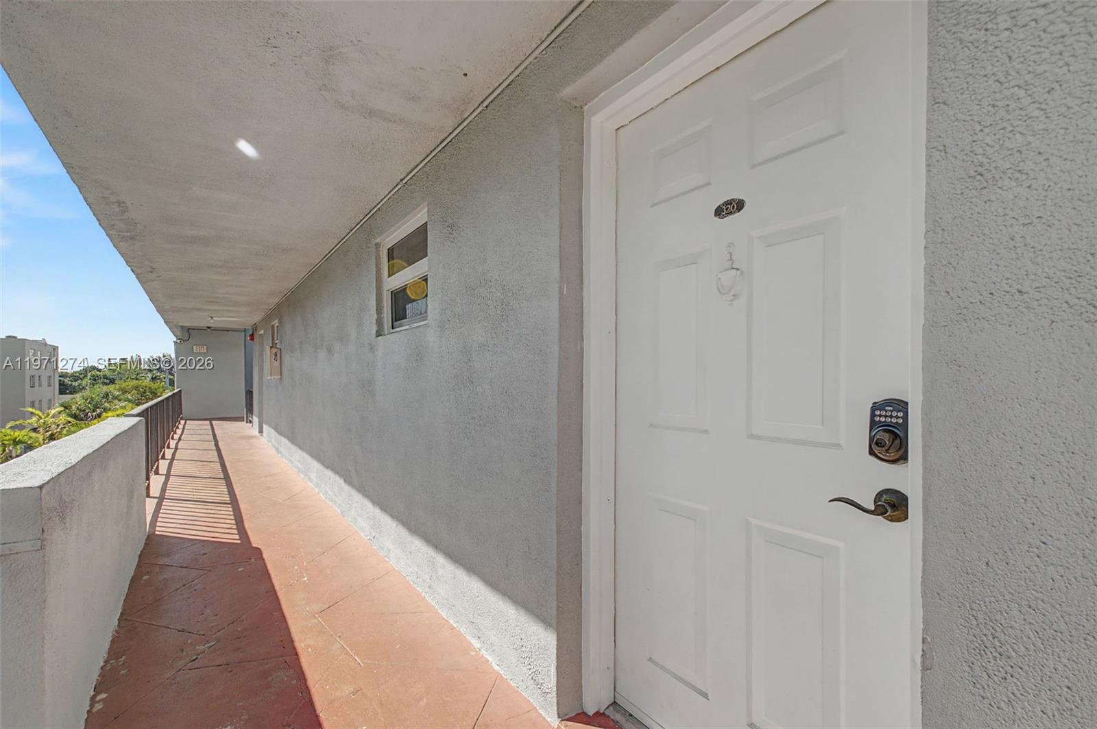 An exterior view of an apartment building walkway with a white door and keypad lock — 399 NW 72nd Ave # 320, Miami FL 33126, MIAMI, FL