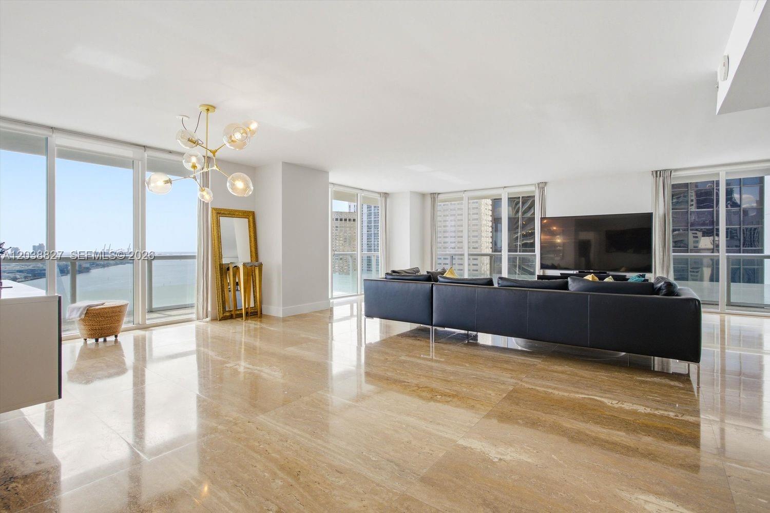 A modern living room features a black sectional sofa, circular ottoman, and polished marble floors — 50 Biscayne Blvd # 2510, Miami FL 33132, MIAMI, FL