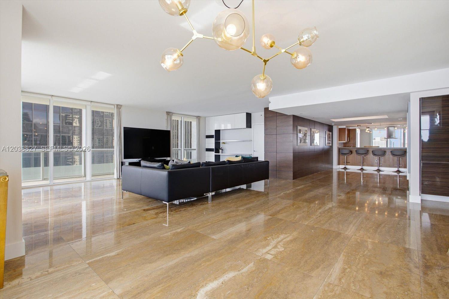 A modern living room features polished stone floors, a black sectional sofa, and a chandelier — 50 Biscayne Blvd # 2510, Miami FL 33132, MIAMI, FL