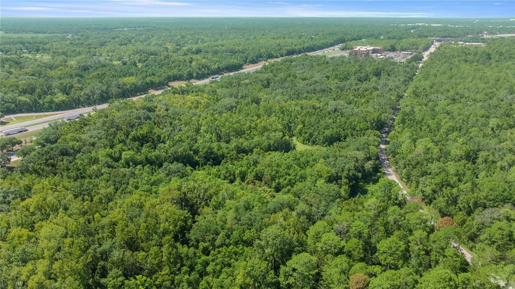 An aerial view shows a dense forest area adjacent to a highway and a commercial building — 6226 SW 34TH STREET, GAINESVILLE, FL