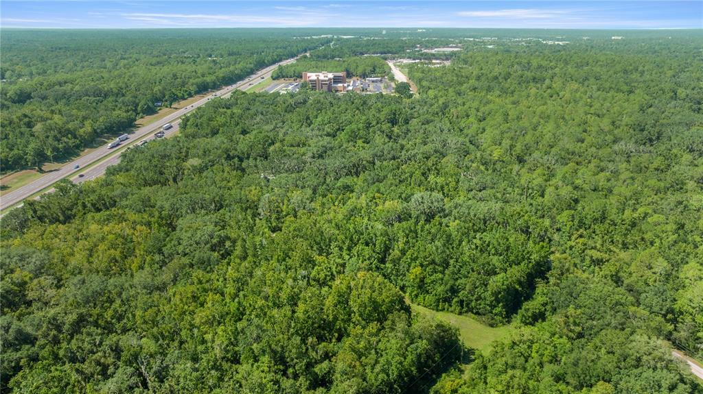 An aerial view shows a large, wooded plot of land next to a highway and buildings — 6226 SW 34TH STREET, GAINESVILLE, FL
