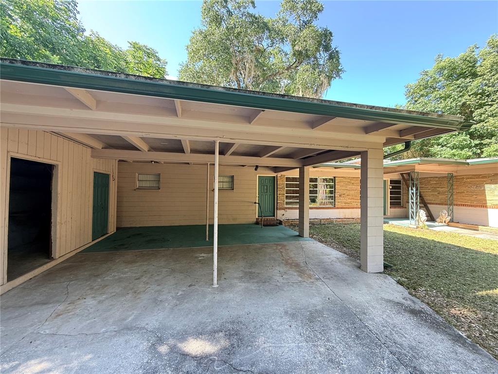 A concrete carport with a green floor and exposed beams attached to a house exterior — 816 NW 14TH AVE., GAINESVILLE, FL