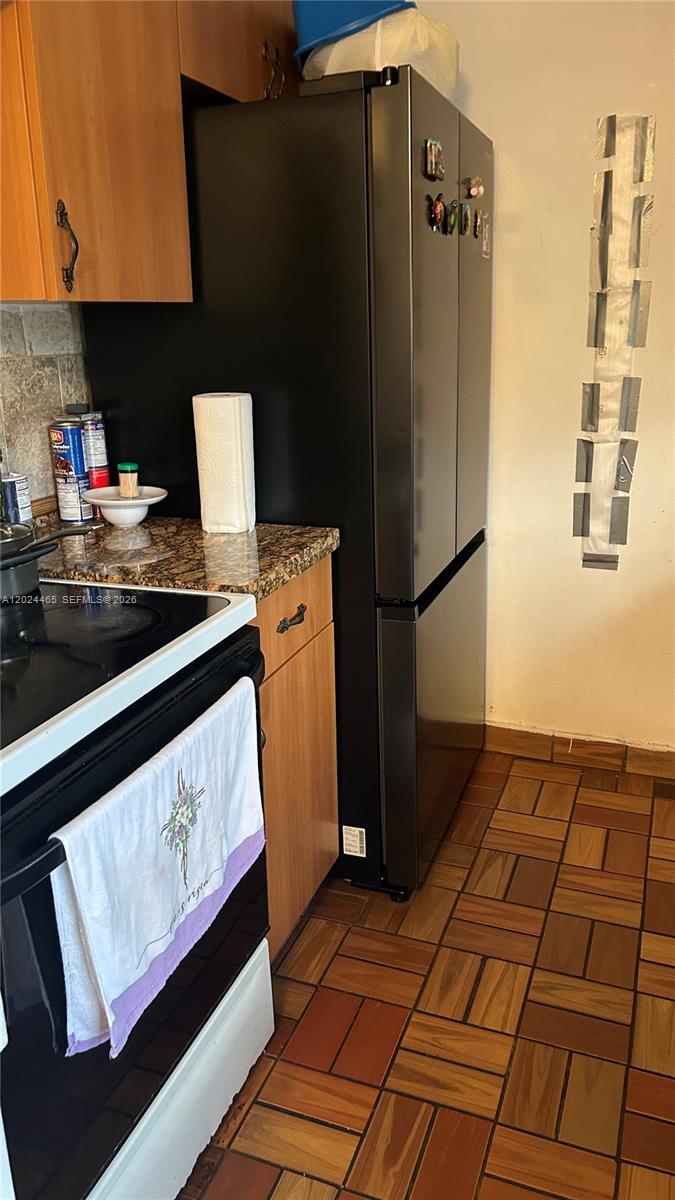 A kitchen features a black refrigerator, wood cabinets, granite countertops, and a tiled floor — 11750 SW 186th St, Miami FL 33177, MIAMI, FL