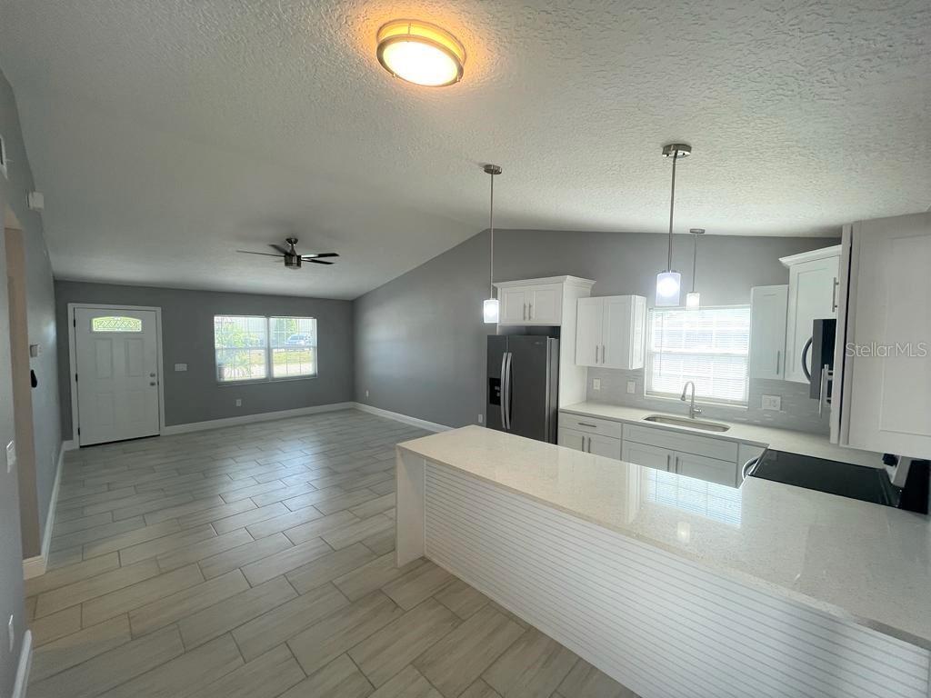 An open-concept kitchen and living area featuring white cabinets, quartz countertops, and light-colored tile flooring — 130 E 17TH STREET UNIT 132, ST CLOUD, FL