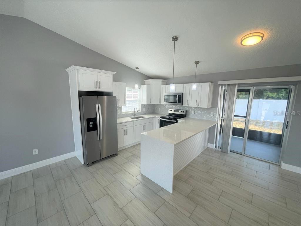 A modern kitchen features white cabinets, stainless steel appliances, quartz countertops, and light tile flooring — 130 E 17TH STREET UNIT 132, ST CLOUD, FL