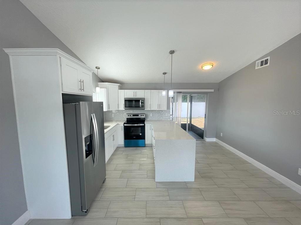 A modern kitchen features white cabinets, stainless steel appliances, a quartz island, and tile flooring — 130 E 17TH STREET UNIT 132, ST CLOUD, FL
