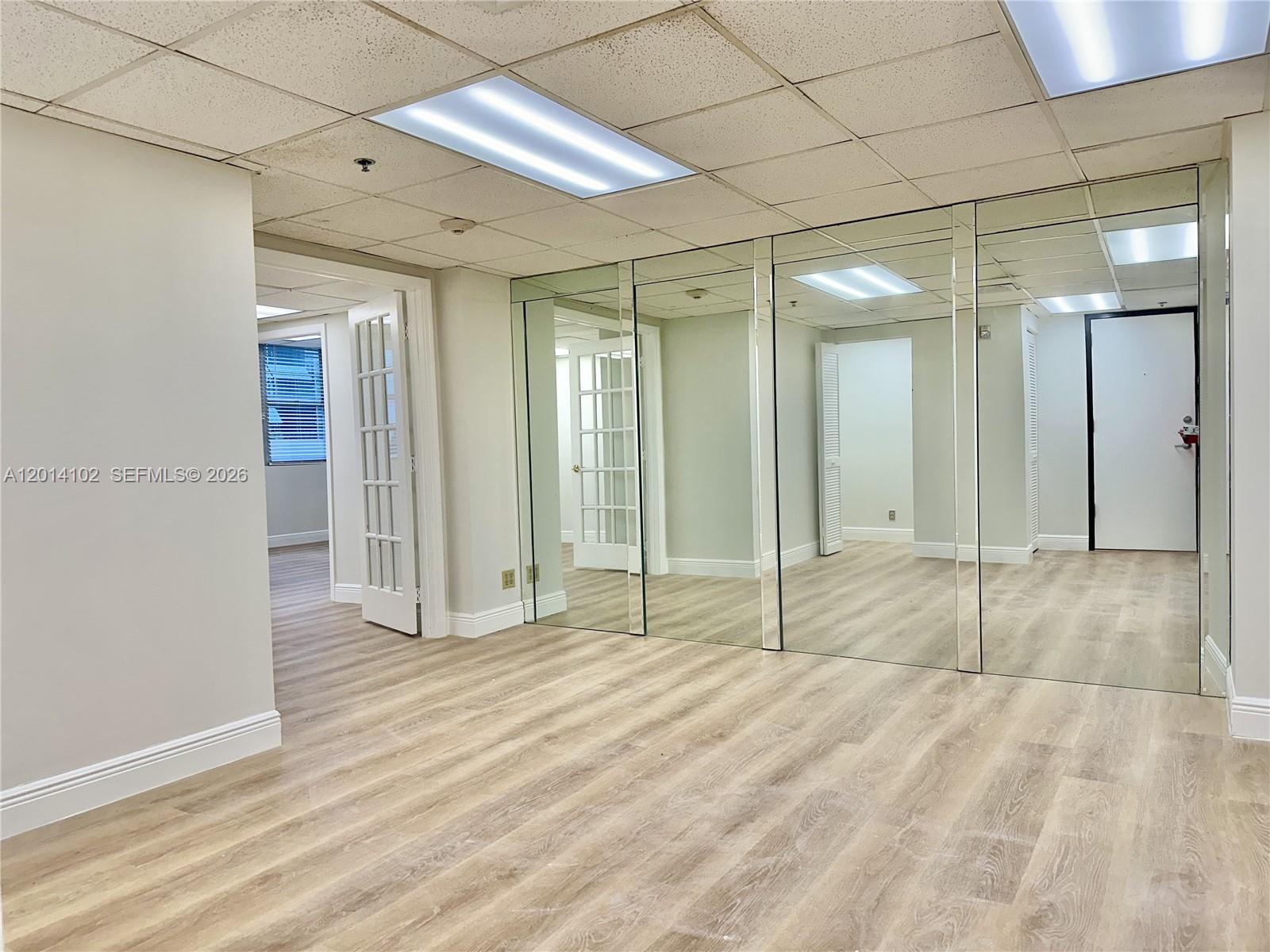 An office room features light wood-look flooring, a drop ceiling, and a mirrored wall — 825 Brickell Bay Dr # 1751, Miami FL 33131, MIAMI, FL