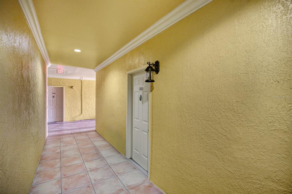 A bright yellow hallway features tiled flooring, a white door, and a wall-mounted light fixture — 4311 BAYSIDE VILLAGE DRIVE UNIT 303, TAMPA, FL