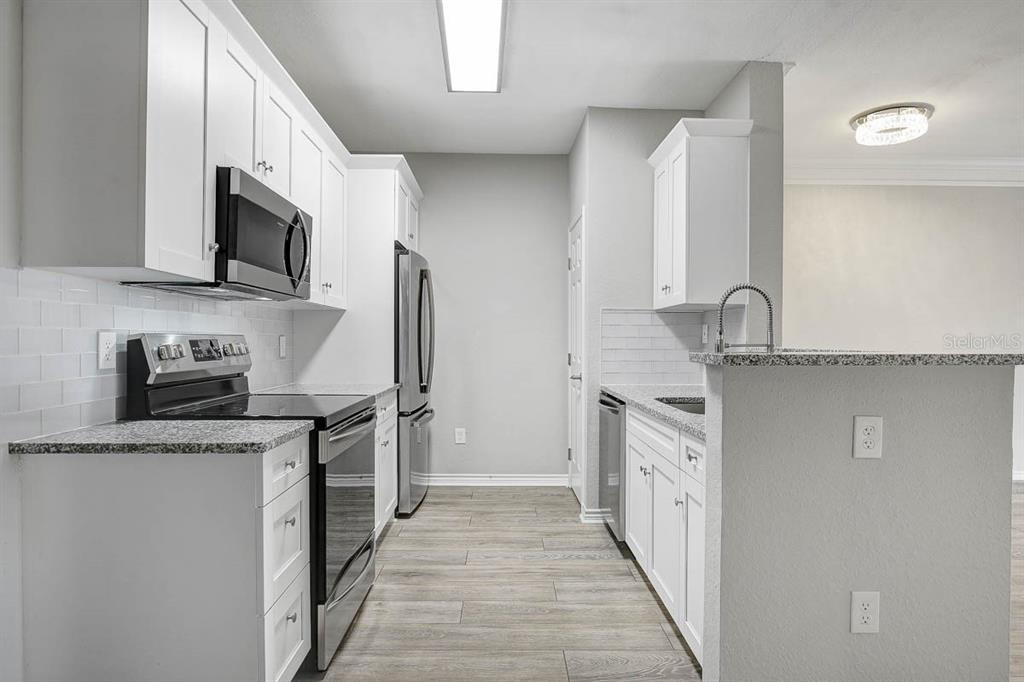 A kitchen features white cabinets, stainless steel appliances, granite countertops, and a subway tile backsplash — 4311 BAYSIDE VILLAGE DRIVE UNIT 303, TAMPA, FL