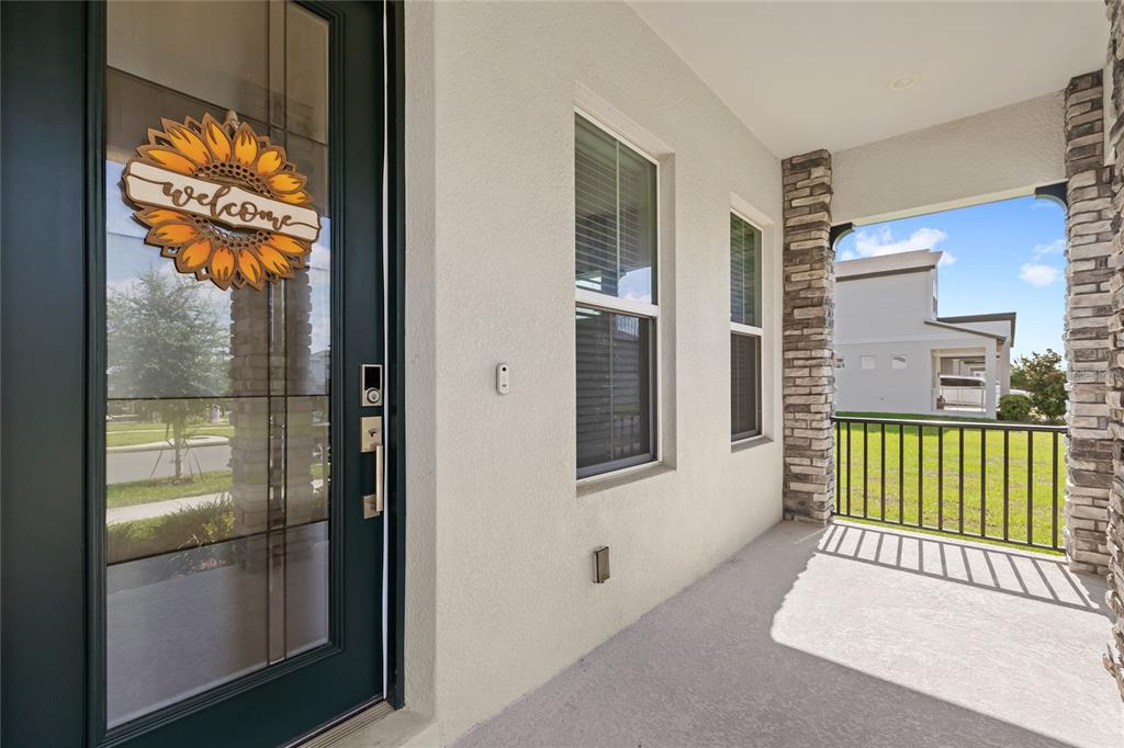 A covered front porch features a dark glass door with a sunflower sign and stone pillars — 16043 SILVER BROOK WAY, WINTER GARDEN, FL