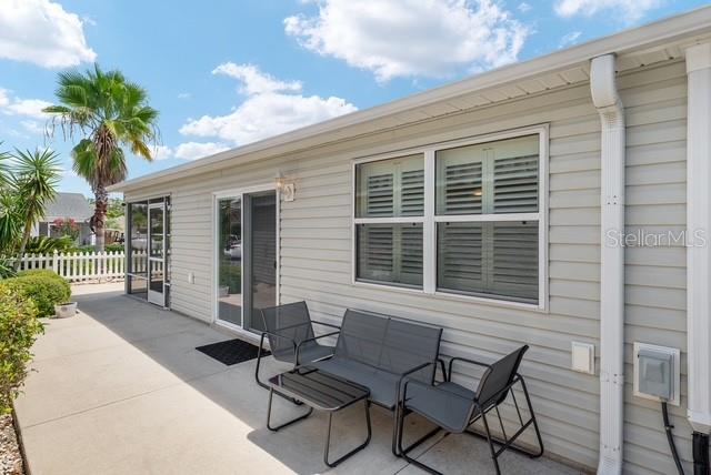 A patio with outdoor furniture sits beside a house with light-colored siding and shutters — 1636 ABASCO COURT, THE VILLAGES, FL