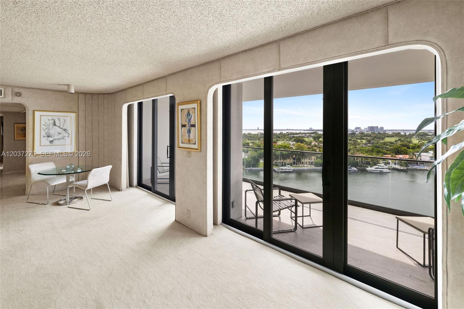 A living area with beige carpet, glass dining table, and sliding doors leading to a balcony — 5500 Collins Ave # 1401, Miami Beach FL 33140, MIAMI BEACH, FL